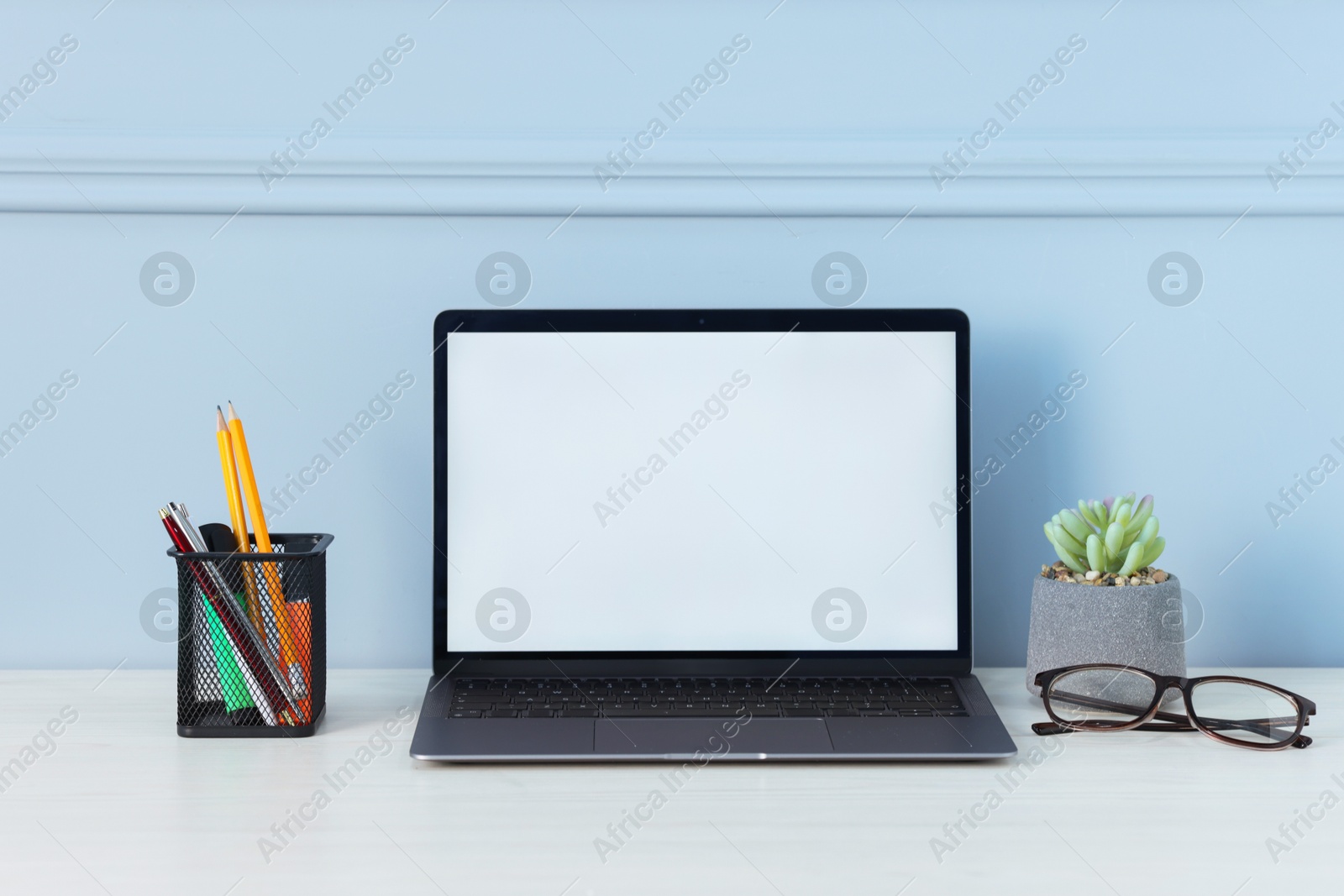 Laptop, stationery, glasses and floral decor on office table near light wall Photo of Laptop, stationery, glasses and floral decor on office table near light wall