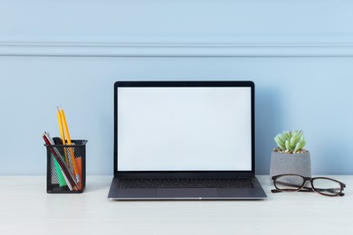 Photo of Laptop, stationery, glasses and floral decor on office table near light wall