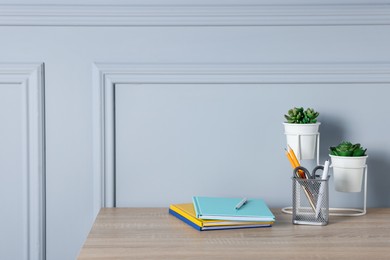 Photo of Different stationery and floral decor on wooden office table near light wall, space for text