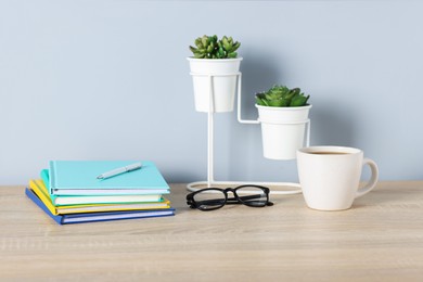Photo of Different stationery, glasses, coffee and floral decor on wooden office table near light wall