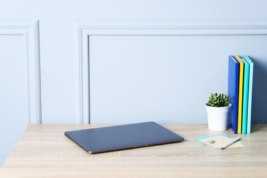 Photo of Laptop, stationery and floral decor on wooden office table near light wall