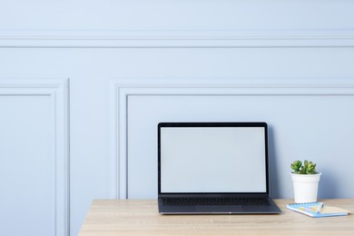 Photo of Laptop, stationery and floral decor on wooden office table near light wall, space for text