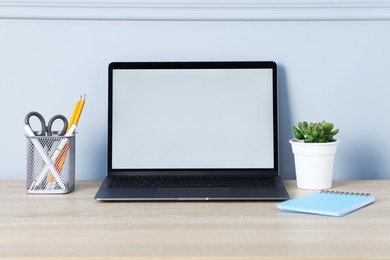 Photo of Laptop, stationery and floral decor on wooden office table near light wall