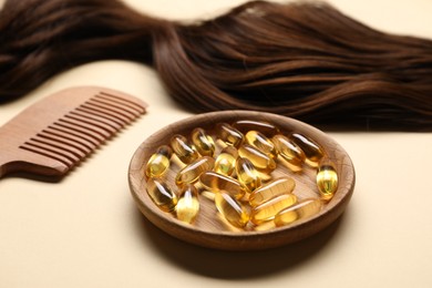 Photo of Collagen capsules, hair lock and comb on beige background, closeup