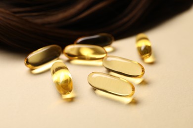 Photo of Collagen capsules and hair lock on beige background, closeup