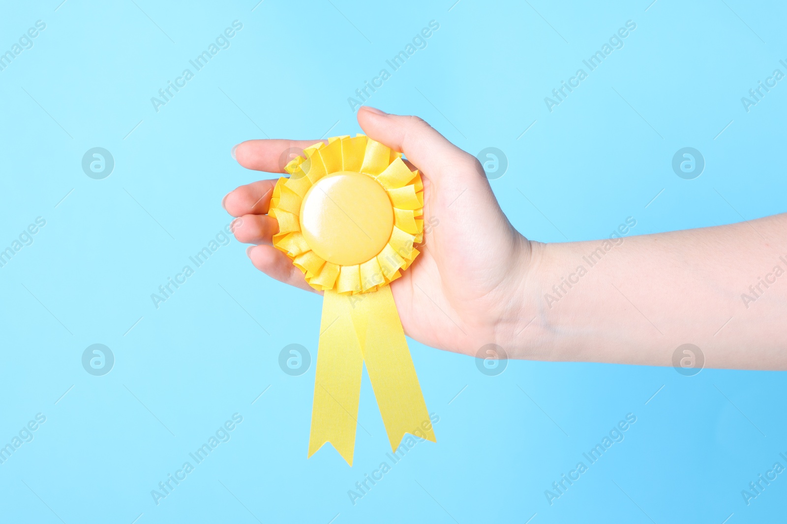 Woman holding yellow award ribbon on light blue background, closeup Photo of Woman holding yellow award ribbon on light blue background, closeup