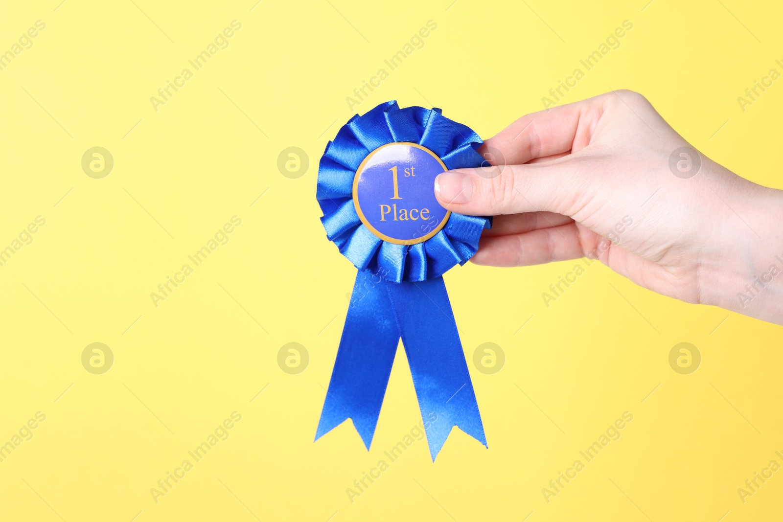 Woman holding blue award ribbon on yellow background, closeup Photo of Woman holding blue award ribbon on yellow background, closeup