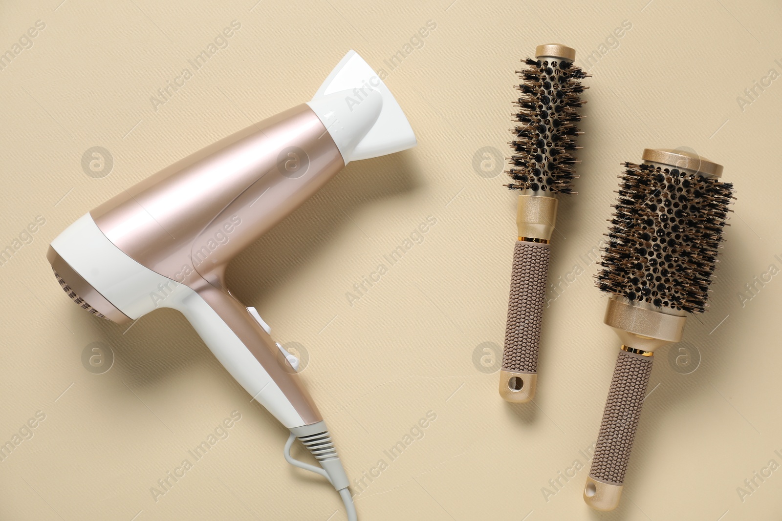 Round brushes and dryer on beige background, flat lay Photo of Round brushes and dryer on beige background, flat lay