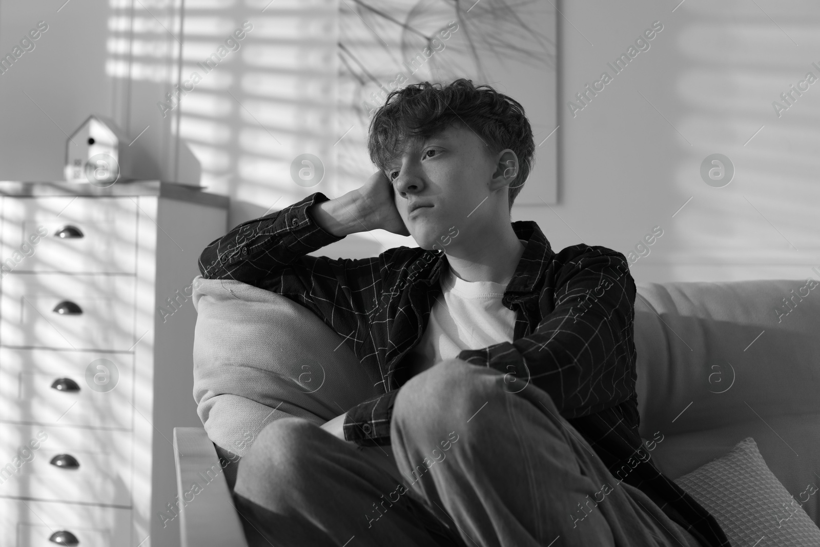 Teen problems. Depressed teenage boy on sofa at home. Black and white effect Photo of Teen problems. Depressed teenage boy on sofa at home. Black and white effect