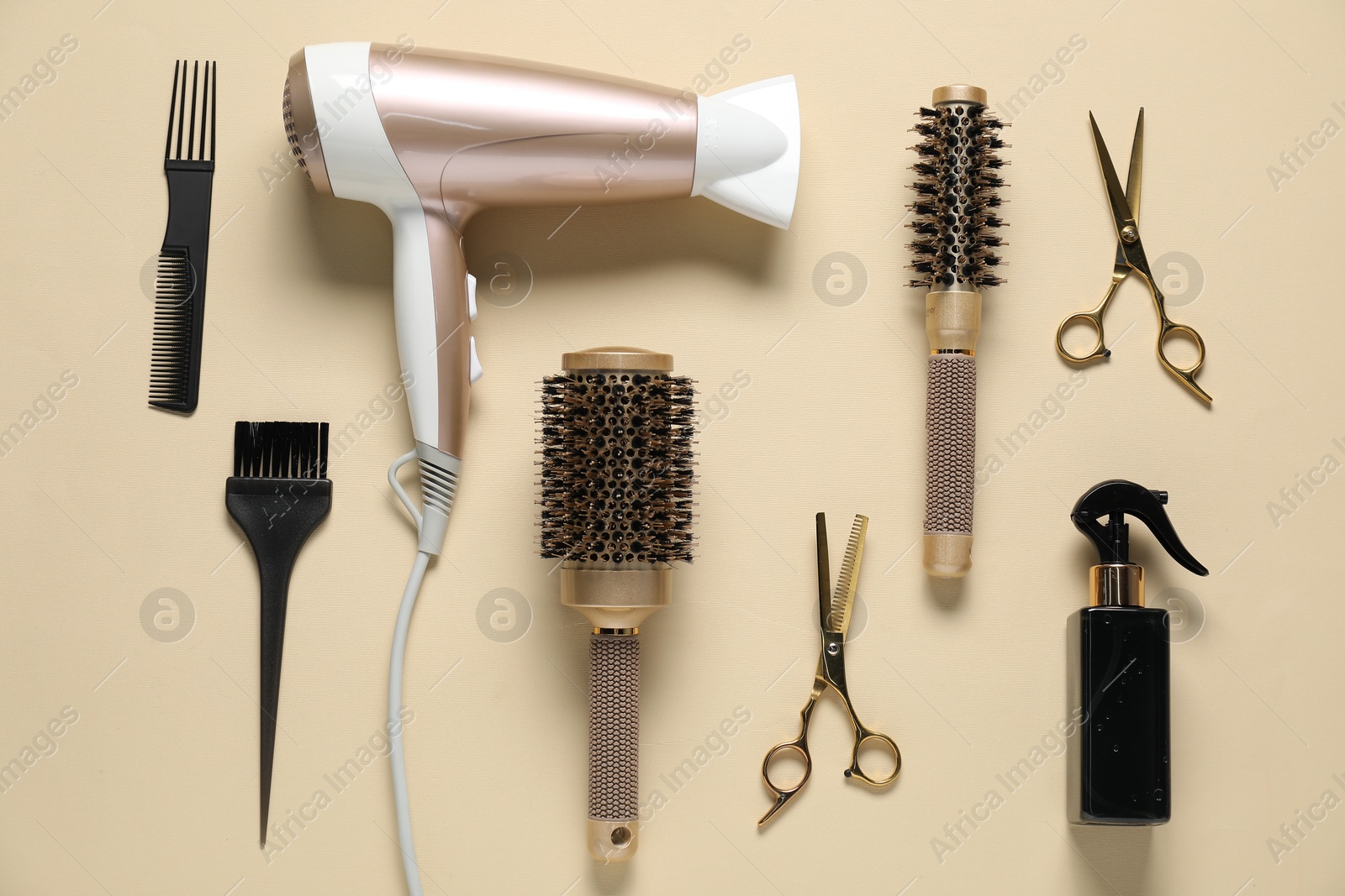 Photo of Round brushes, dryer and other hairdresser's tools on beige background, flat lay