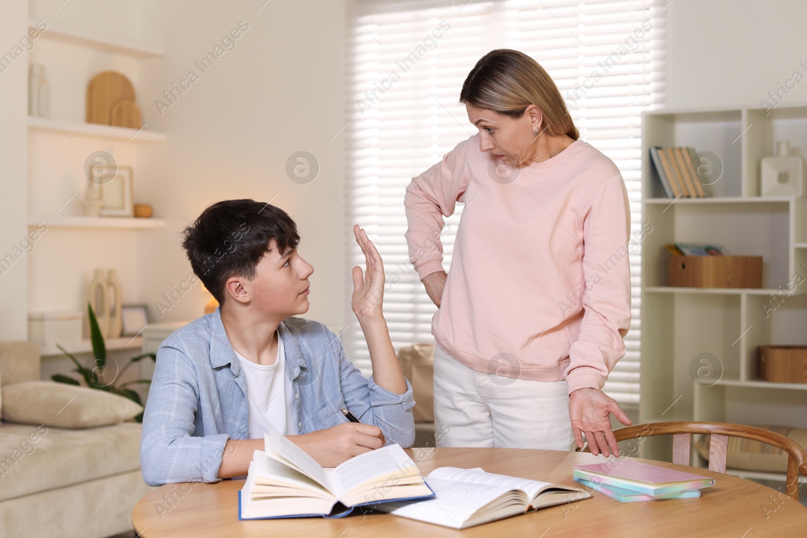 Annoyed mother and her stressful son doing homework at table indoors Photo of Annoyed mother and her stressful son doing homework at table indoors