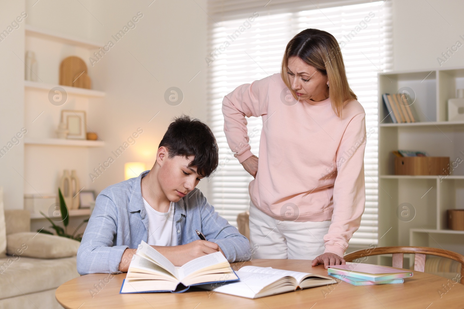 Annoyed mother and her stressful son doing homework at table indoors Photo of Annoyed mother and her stressful son doing homework at table indoors