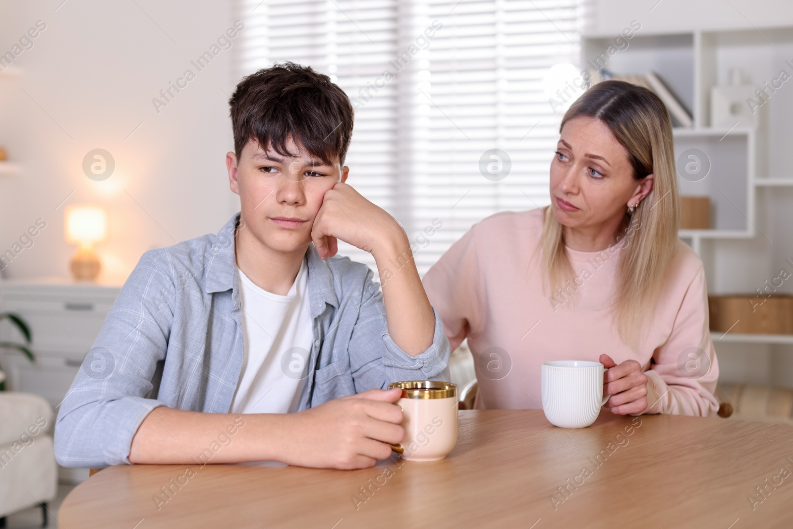 Mother consoling her upset son at table indoors Photo of Mother consoling her upset son at table indoors