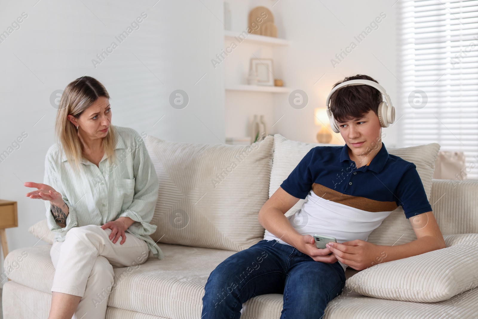 Teenage son in headphones with smartphone ignoring his mother at home Photo of Teenage son in headphones with smartphone ignoring his mother at home