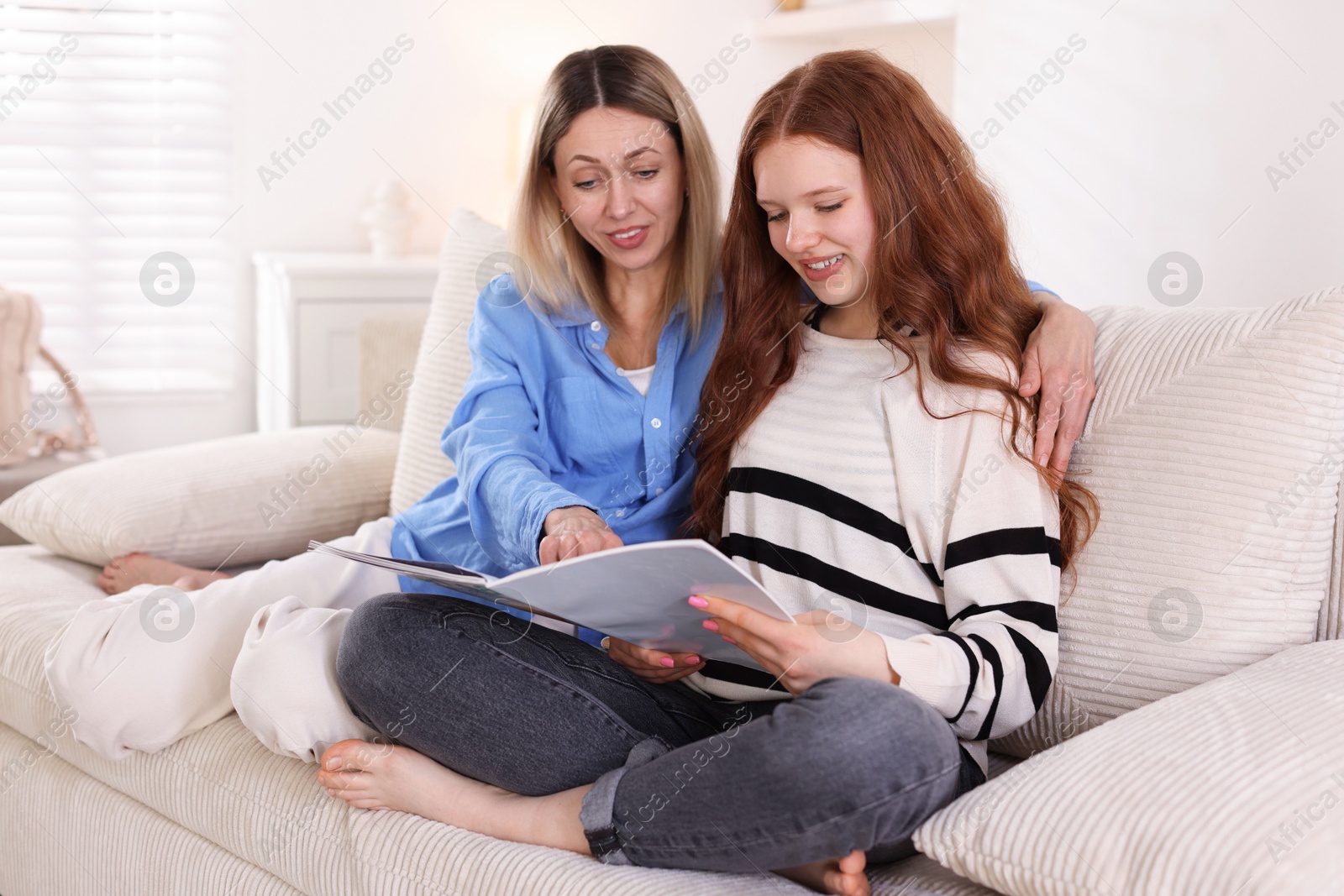 Photo of Mother and her daughter reading magazine on sofa at home