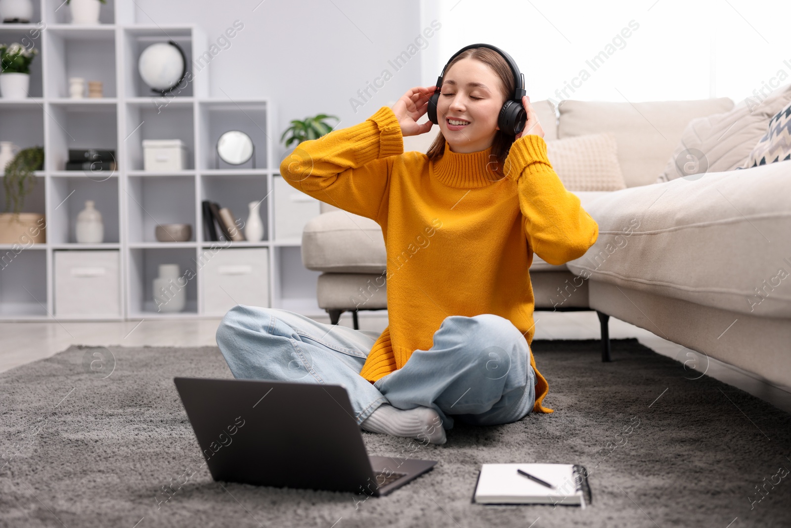 Teenage girl in headphones listening to music near laptop on floor at home Photo of Teenage girl in headphones listening to music near laptop on floor at home