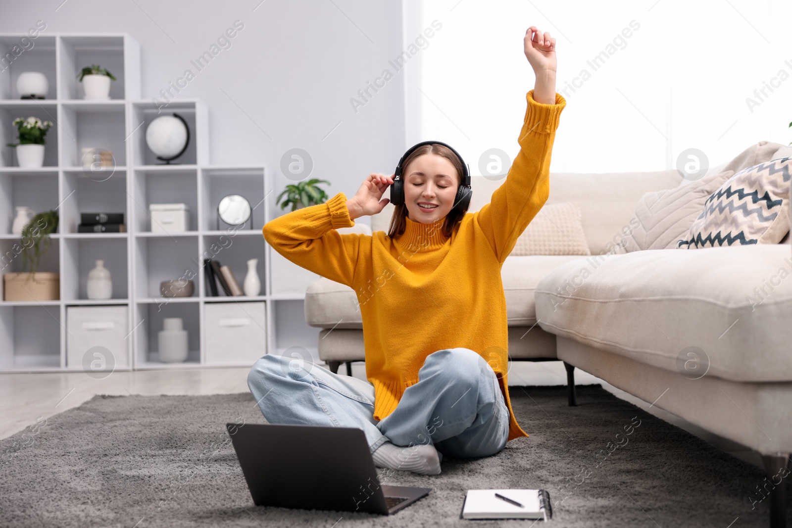 Teenage girl in headphones listening to music near laptop on floor at home Photo of Teenage girl in headphones listening to music near laptop on floor at home
