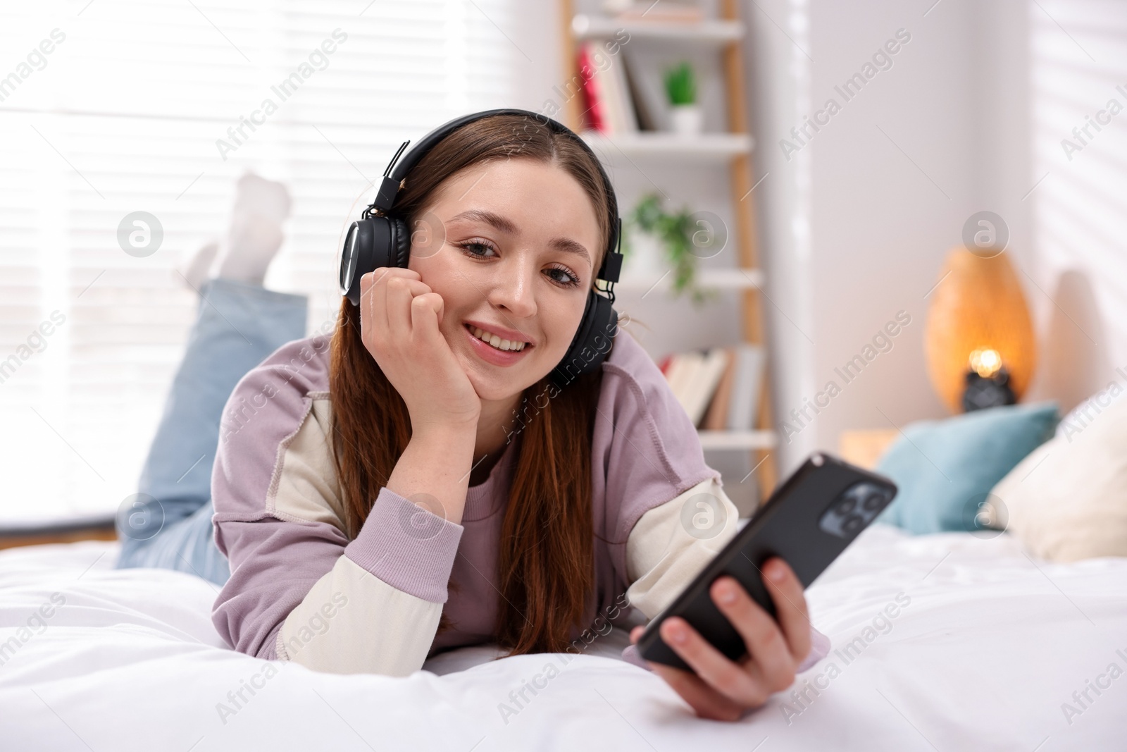 Teenage girl in headphones using smartphone on bed at home Photo of Teenage girl in headphones using smartphone on bed at home