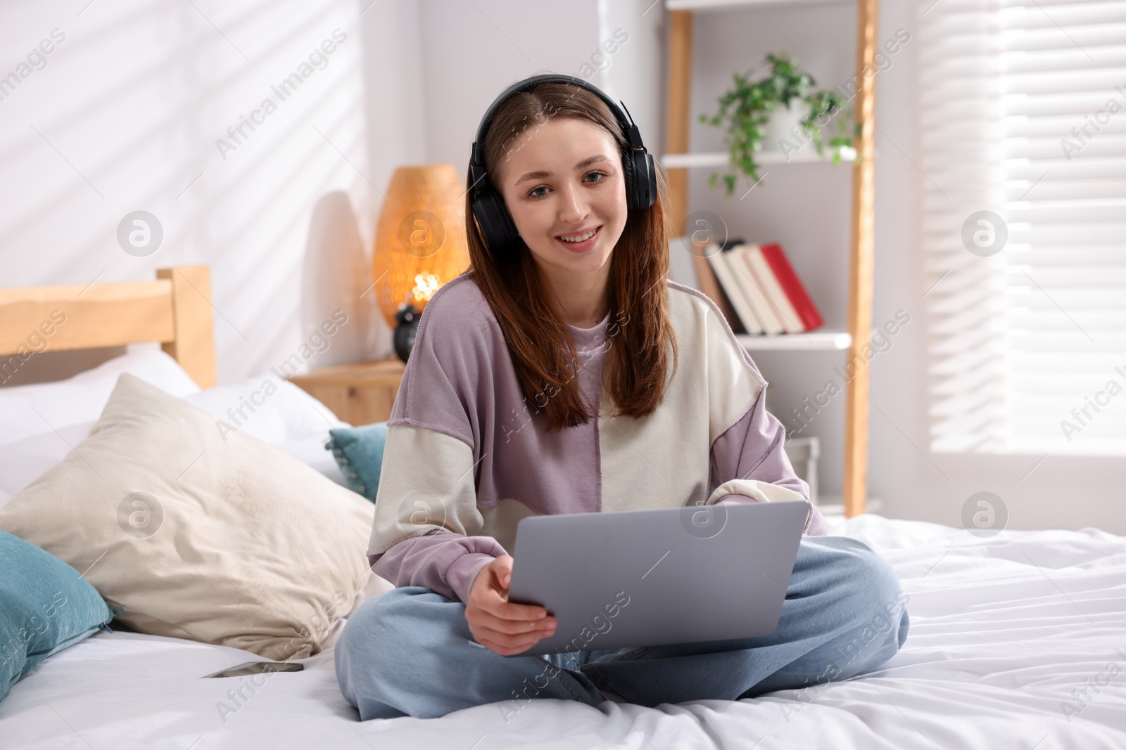 Teenage girl in headphones using laptop on bed at home Photo of Teenage girl in headphones using laptop on bed at home