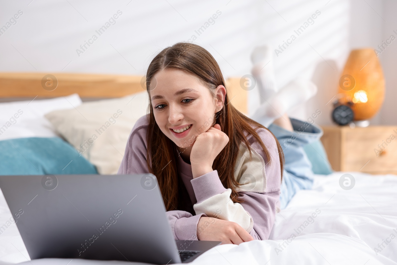 Teenage girl with laptop on bed at home Photo of Teenage girl with laptop on bed at home