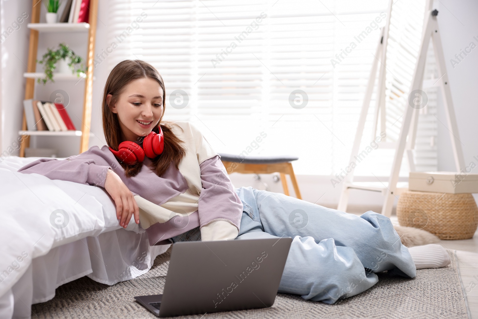 Teenage girl with headphones near laptop on floor at home Photo of Teenage girl with headphones near laptop on floor at home