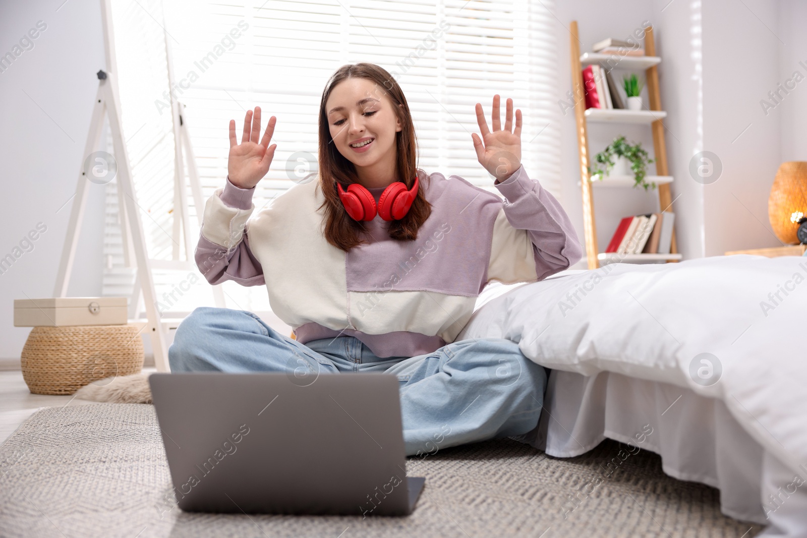 Photo of Teenage girl with headphones having video chat via laptop on floor at home