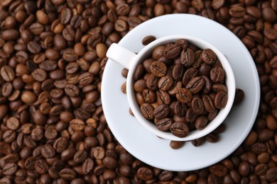 Photo of Cup and saucer on coffee beans, top view. Space for text