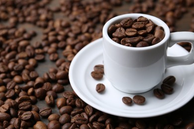 Photo of Aromatic coffee beans, cup and saucer on table, closeup. Space for text