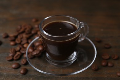 Photo of Aromatic coffee in glass cup and beans on wooden table, closeup