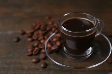 Photo of Aromatic coffee in glass cup and beans on wooden table, closeup. Space for text