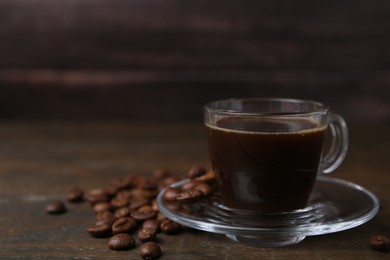 Photo of Aromatic coffee in glass cup and beans on wooden table, closeup. Space for text