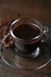 Photo of Aromatic coffee in glass cup and beans on wooden table, closeup