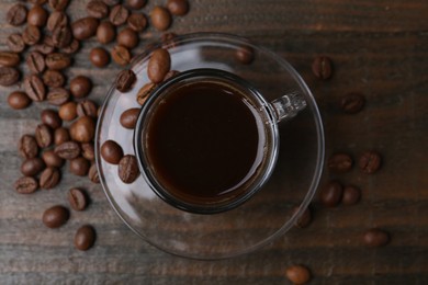 Photo of Aromatic coffee in glass cup and beans on wooden table, flat lay