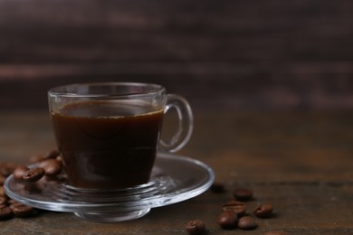 Photo of Aromatic coffee in glass cup and beans on wooden table, closeup. Space for text