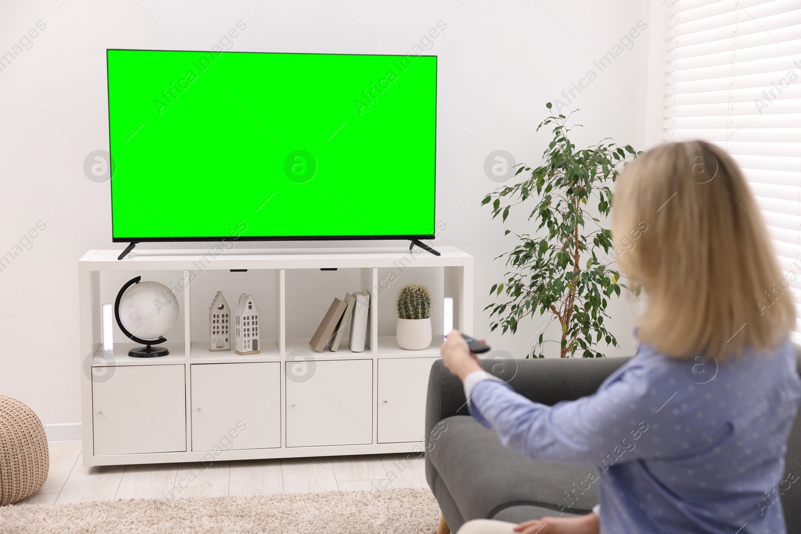 Image of Woman watching modern TV set with green screen in living room. Chroma key compositing