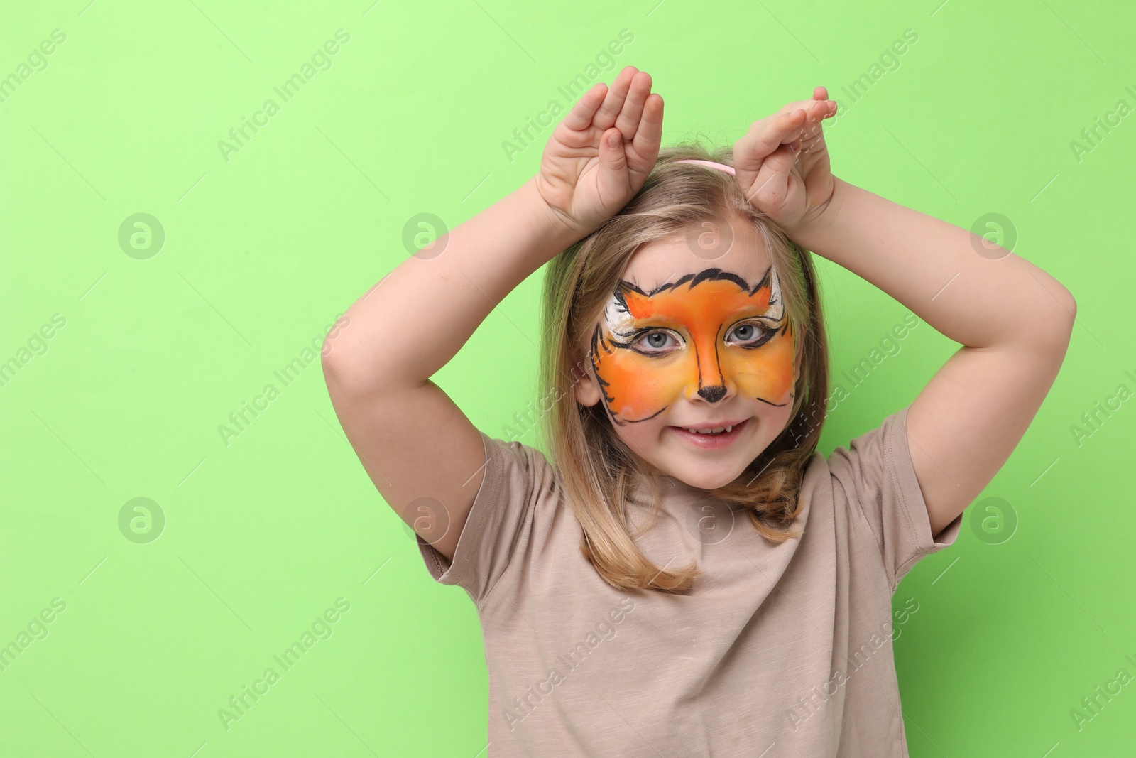 Cute girl with fox face painting posing on light green background Photo of Cute girl with fox face painting posing on light green background