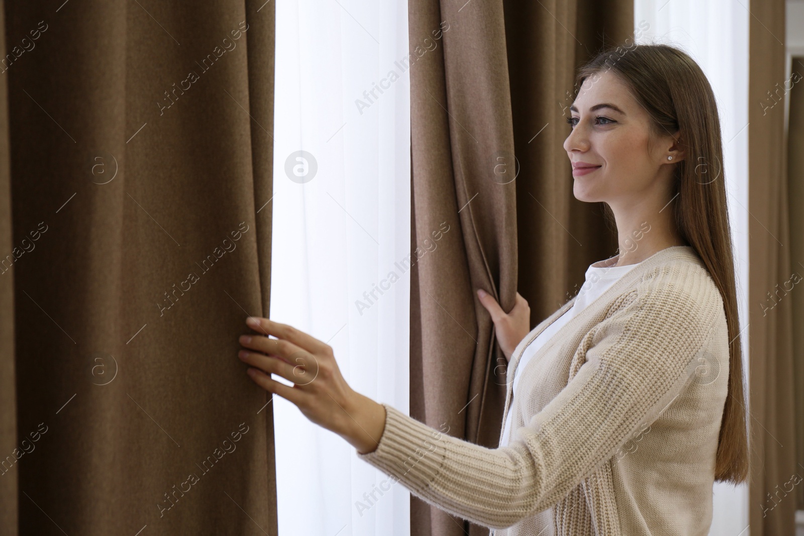 Woman opening elegant window curtains in room Photo of Woman opening elegant window curtains in room