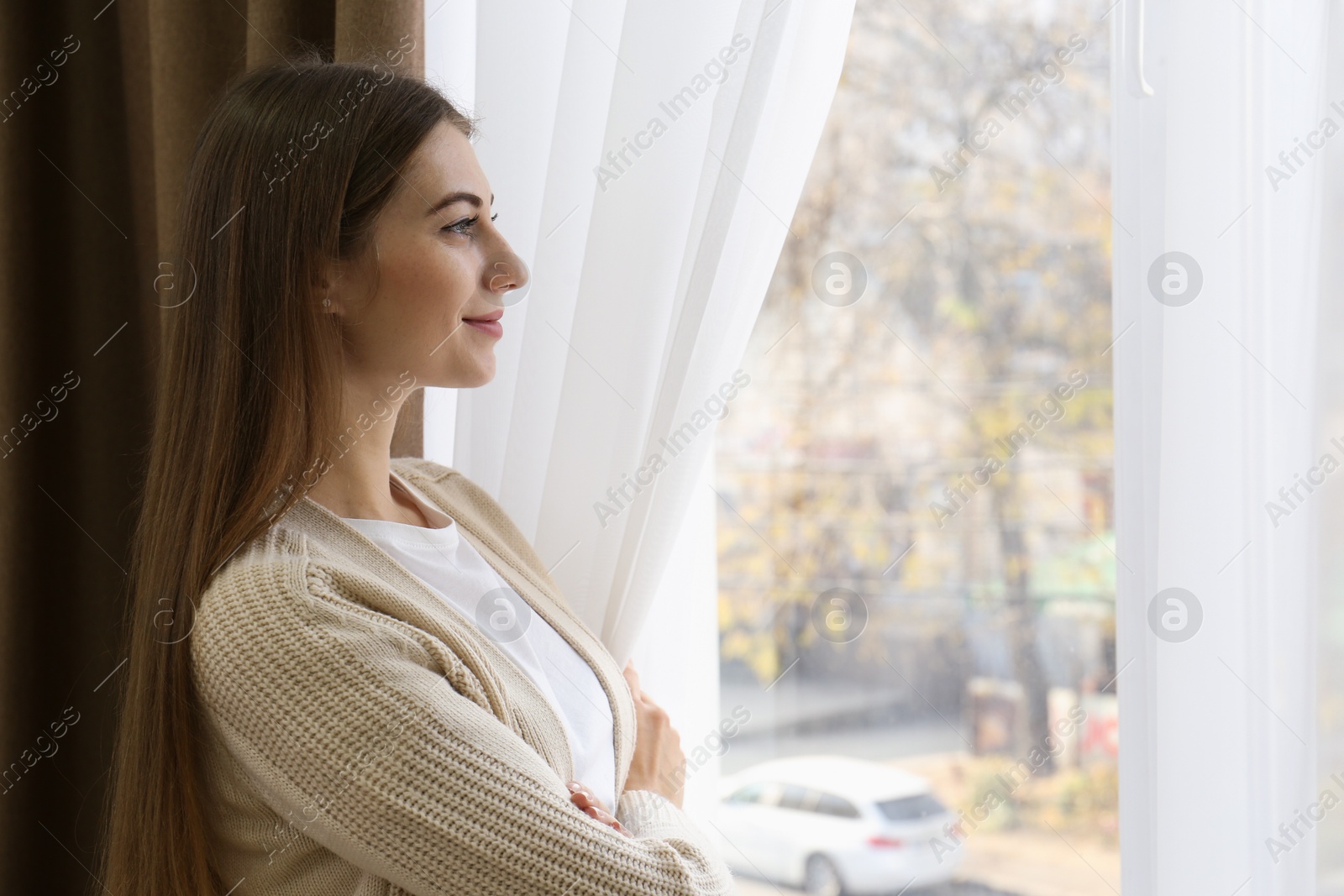 Woman opening elegant window curtains in room Photo of Woman opening elegant window curtains in room