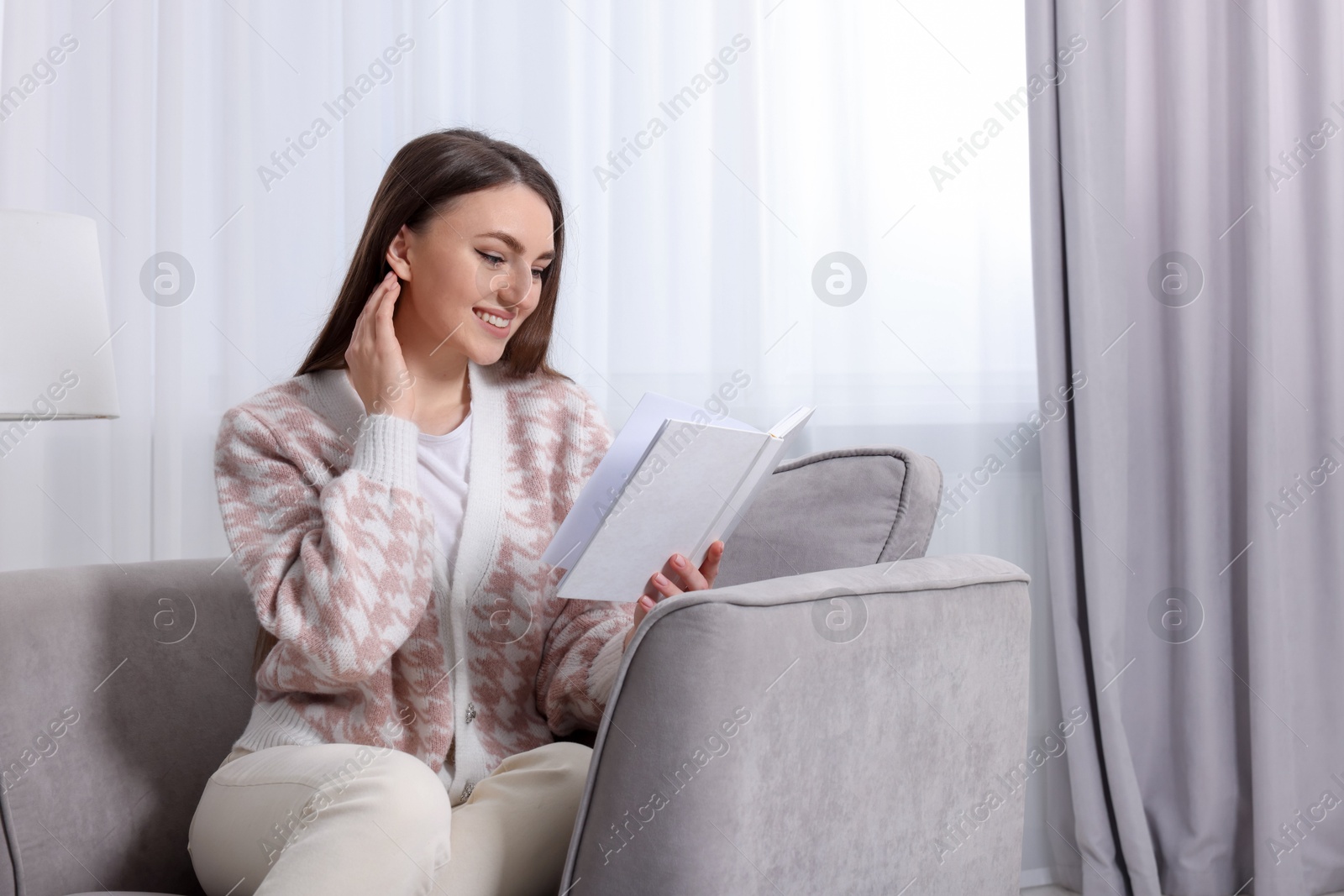 Woman reading book on armchair near window at home Photo of Woman reading book on armchair near window at home