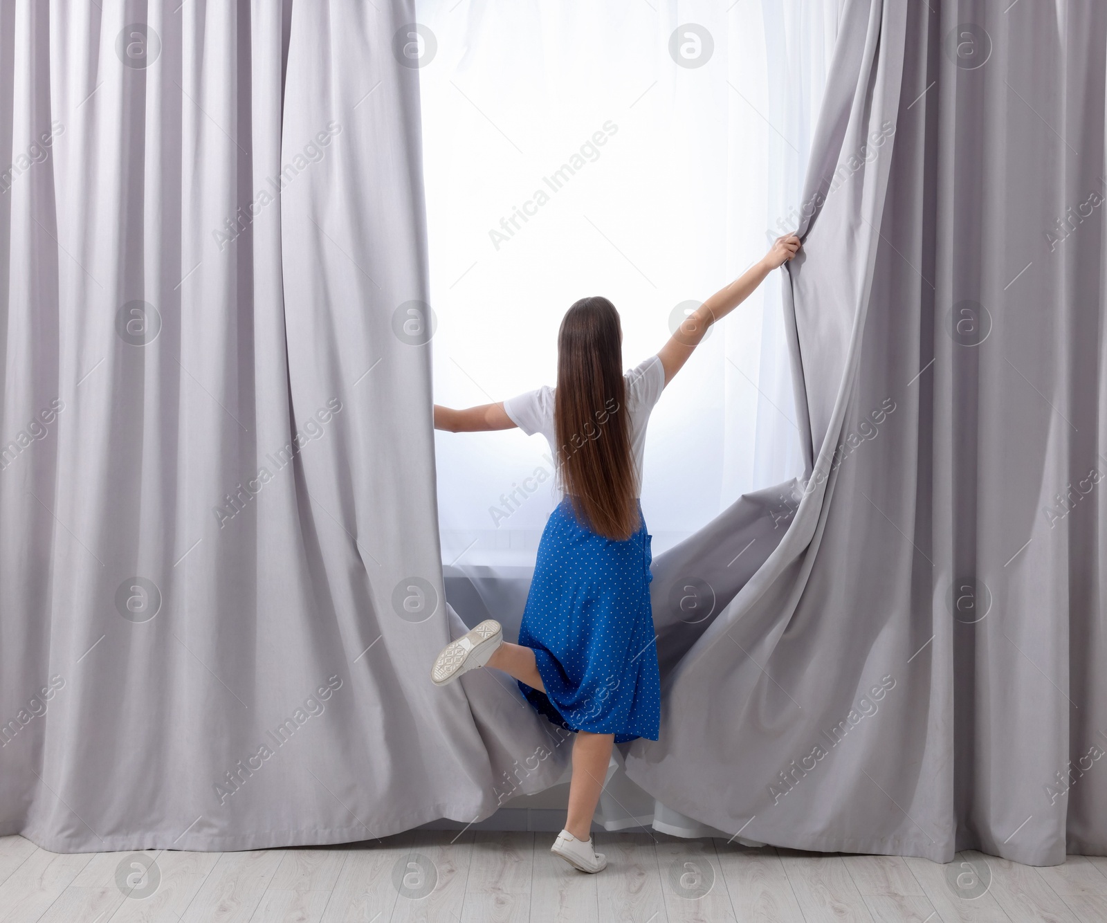 Woman opening stylish curtains at home, back view Photo of Woman opening stylish curtains at home, back view