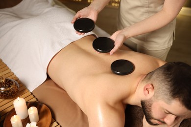 Photo of Man receiving relaxing massage with stones in spa salon