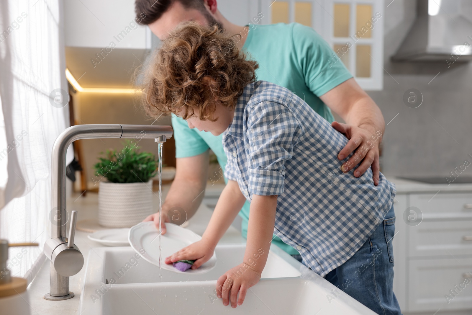 Father and his son washing dishes together in kitchen at home Photo of Father and his son washing dishes together in kitchen at home