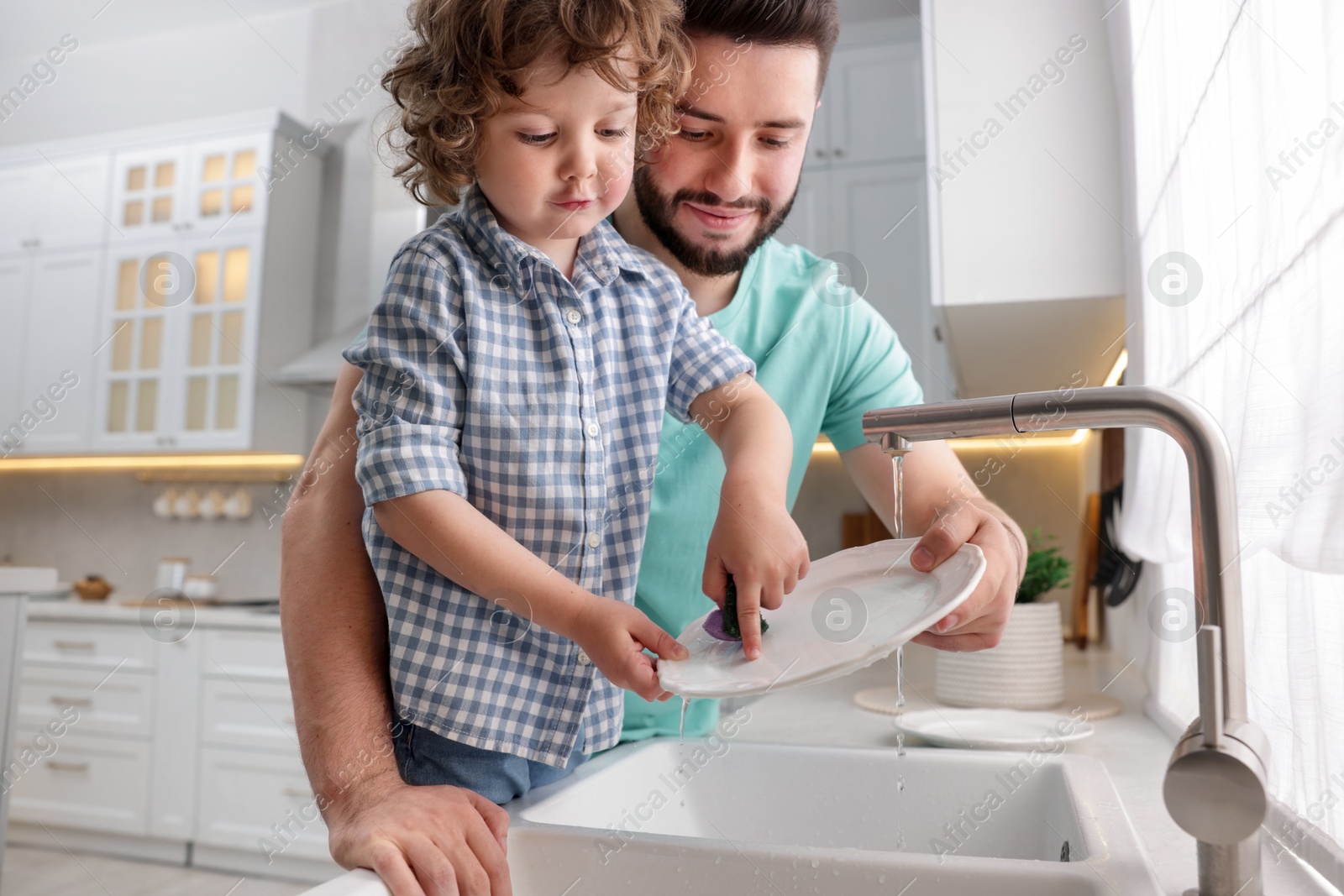 Father and his son washing dishes together in kitchen at home Photo of Father and his son washing dishes together in kitchen at home