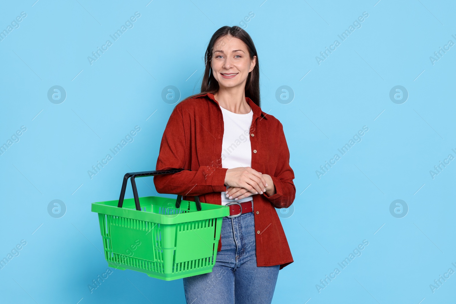 Smiling woman with shopping basket on light blue background Photo of Smiling woman with shopping basket on light blue background