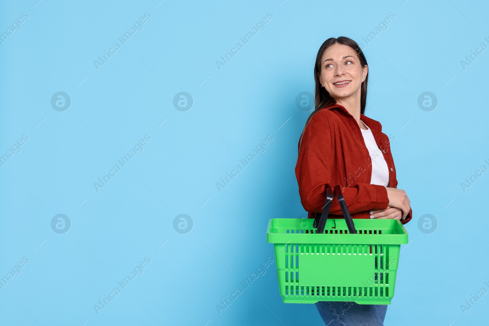 Smiling woman with shopping basket on light blue background. Space for text Photo of Smiling woman with shopping basket on light blue background. Space for text