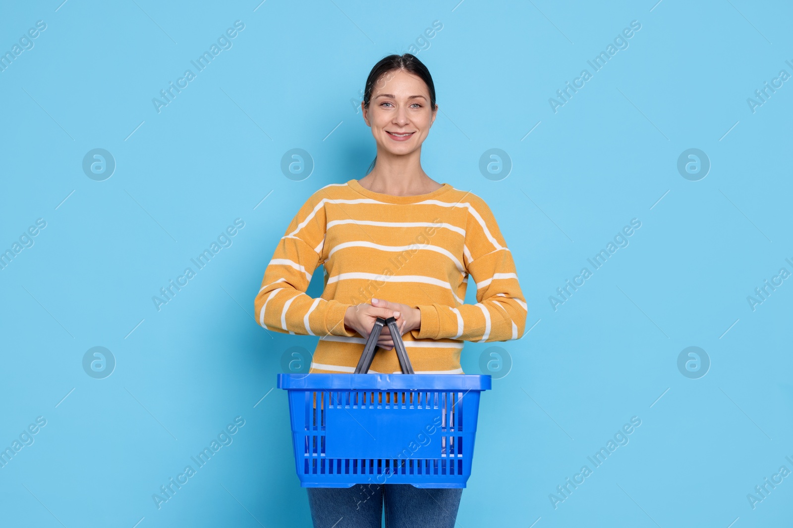 Smiling woman with shopping basket on light blue background Photo of Smiling woman with shopping basket on light blue background