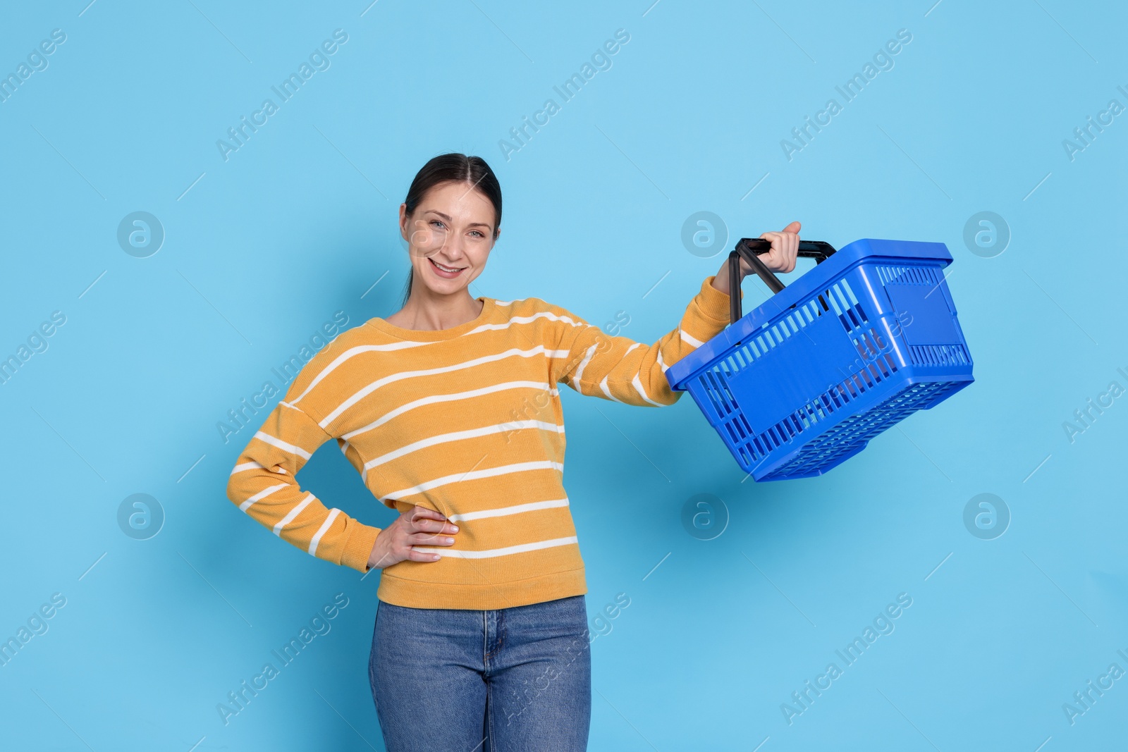Smiling woman with shopping basket on light blue background Photo of Smiling woman with shopping basket on light blue background