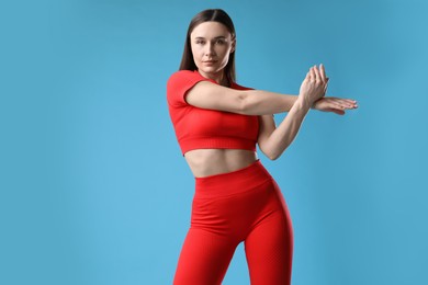 Photo of Woman in sportswear exercising on light blue background, space for text