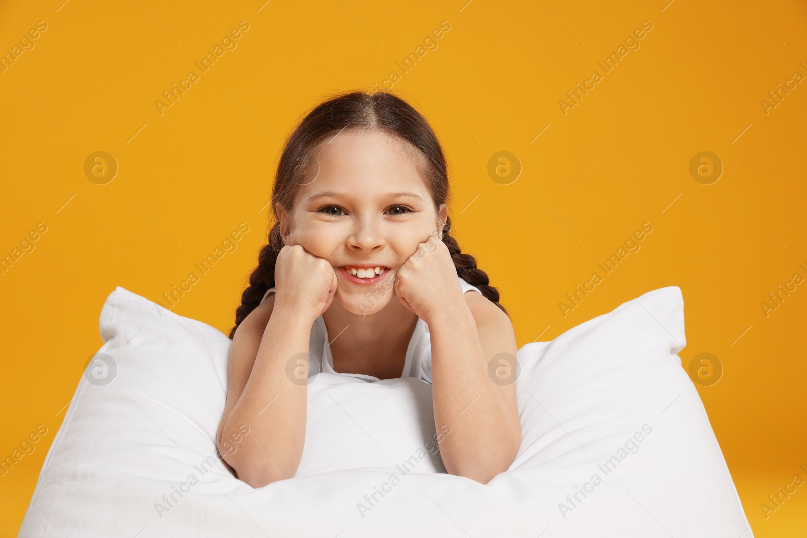 Cute girl with pillow on orange background Photo of Cute girl with pillow on orange background