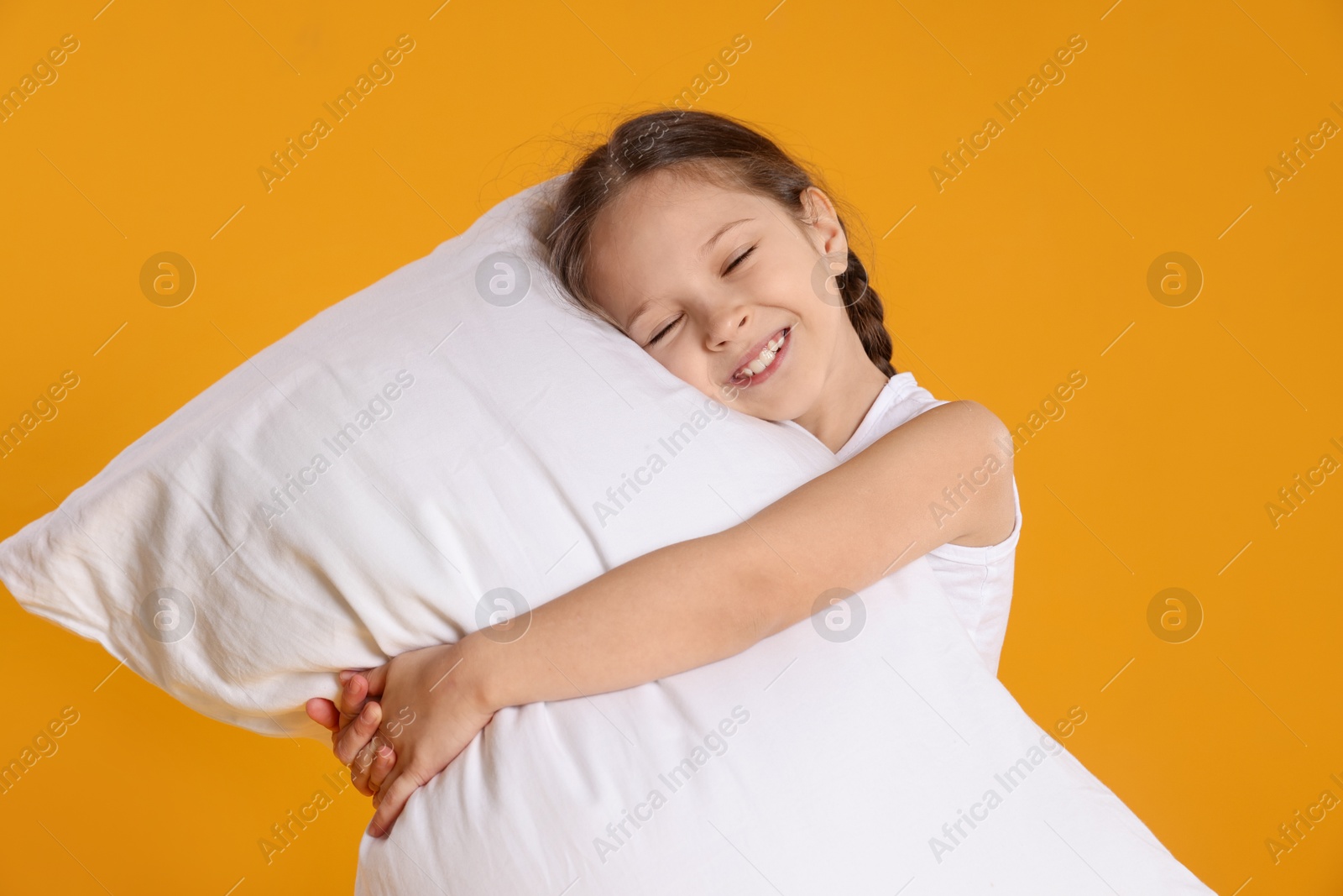 Cute girl with pillow on orange background Photo of Cute girl with pillow on orange background